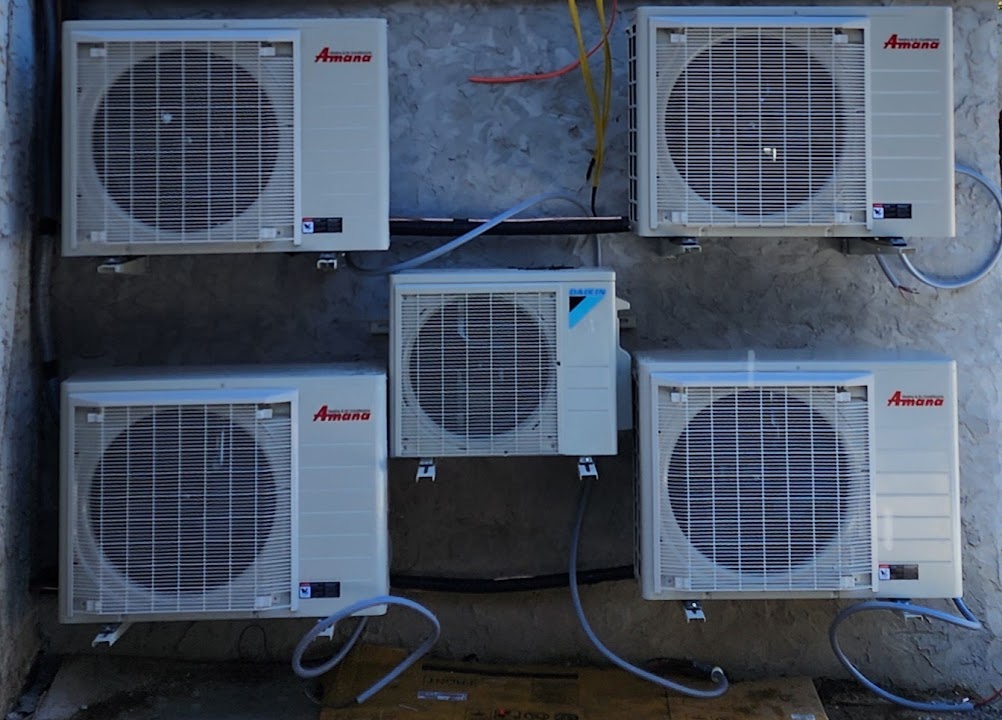 Four Amana S-Series heat pumps and a Daikin mini-split outdoor unit installed beside a renovated home