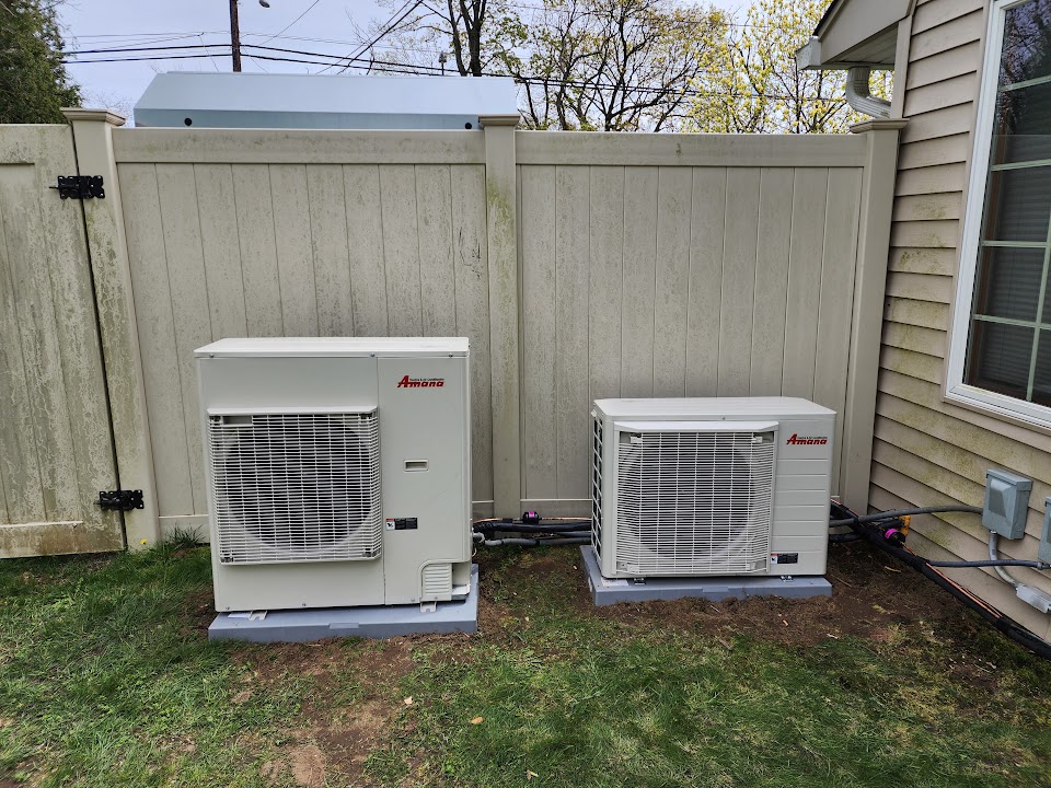Two Amana S-Series heat-pump outdoor units installed beside a fence